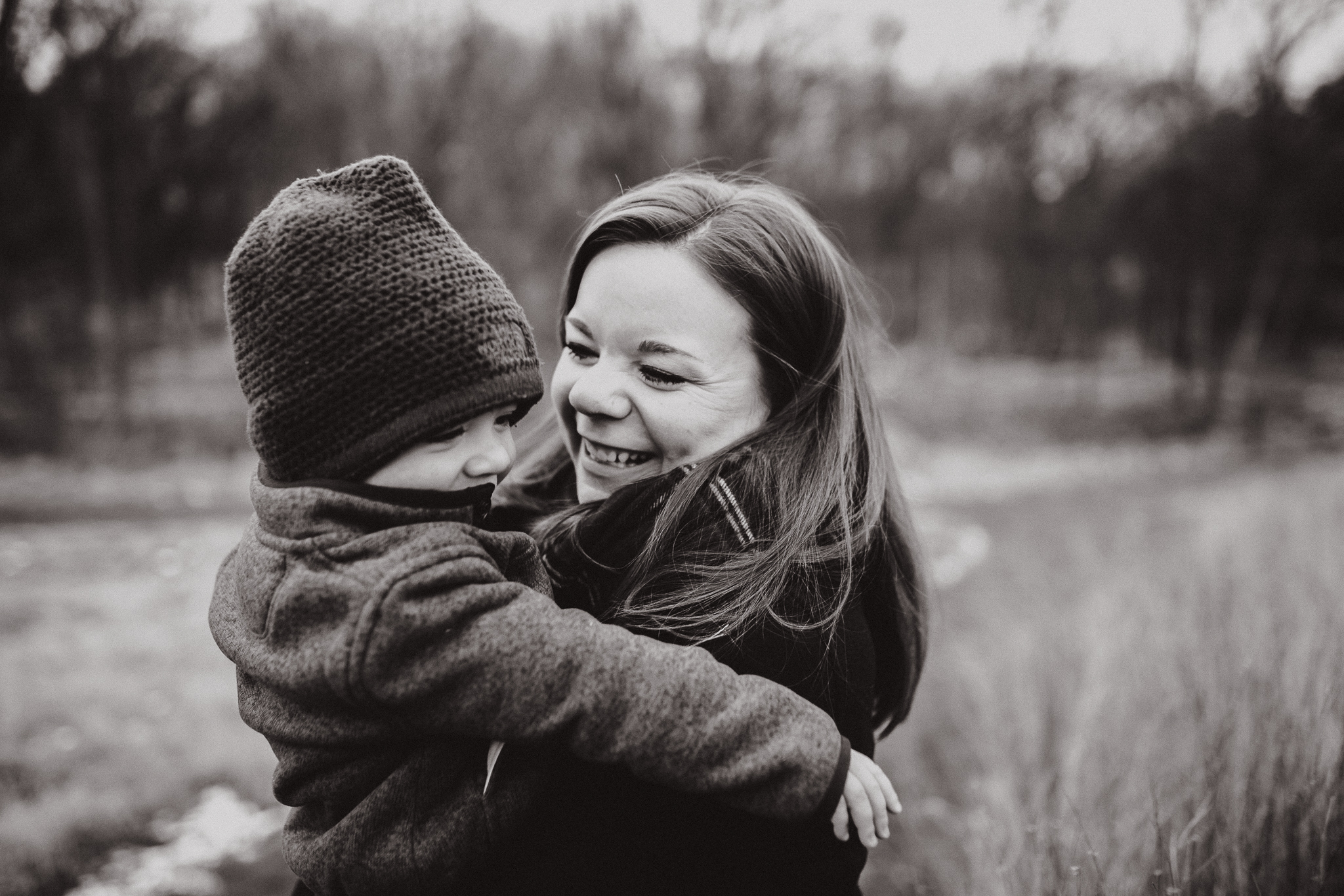 Mother in a plaid scarf swinging her young boy in her arms.